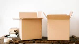 Opened carton boxes and stacked books placed on shabby wooden desk with tape against white wall