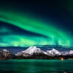 Breathtaking view of aurora borealis illuminating the snowy mountains of Lofoten Islands at night.