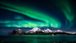 Breathtaking view of aurora borealis illuminating the snowy mountains of Lofoten Islands at night.