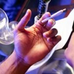 Close-up of hands preparing a cannabis joint with smoking paraphernalia on a table.
