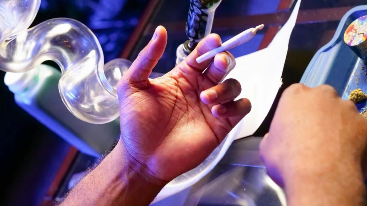 Close-up of hands preparing a cannabis joint with smoking paraphernalia on a table.