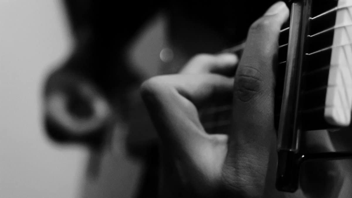 Black and white photo of a guitarist's hands playing an acoustic guitar, emphasizing musical expression.