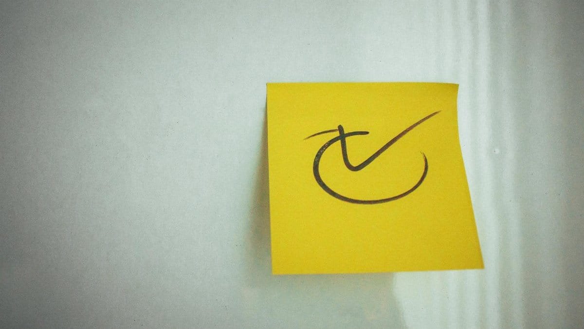 Yellow sticky note with a check mark symbol on a white background, ideal for reminders.