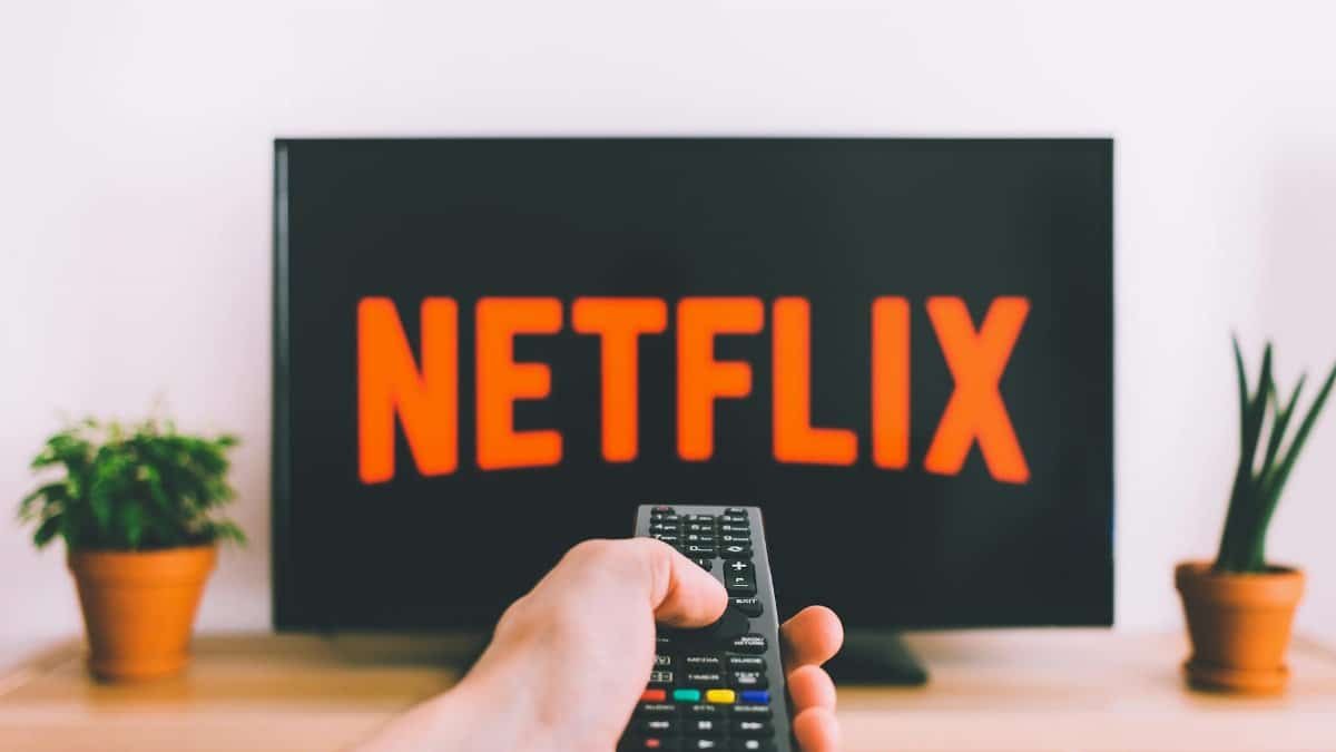A hand holding a TV remote in front of a screen with Netflix, perfect for streaming and movie night themes.