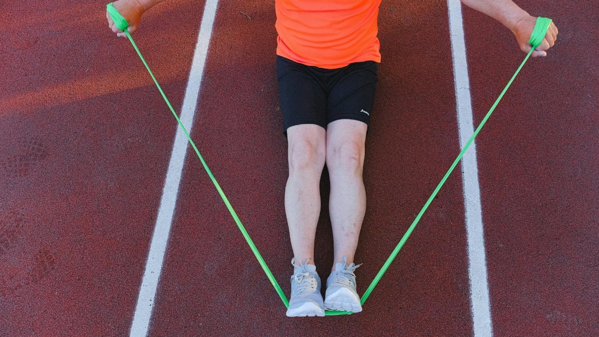 An adult male athlete working out with a green resistance band on a running track. Perfect for fitness and wellness themes.