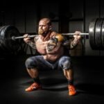 Muscular man lifting heavy weights during an intense squat session inside a gym.