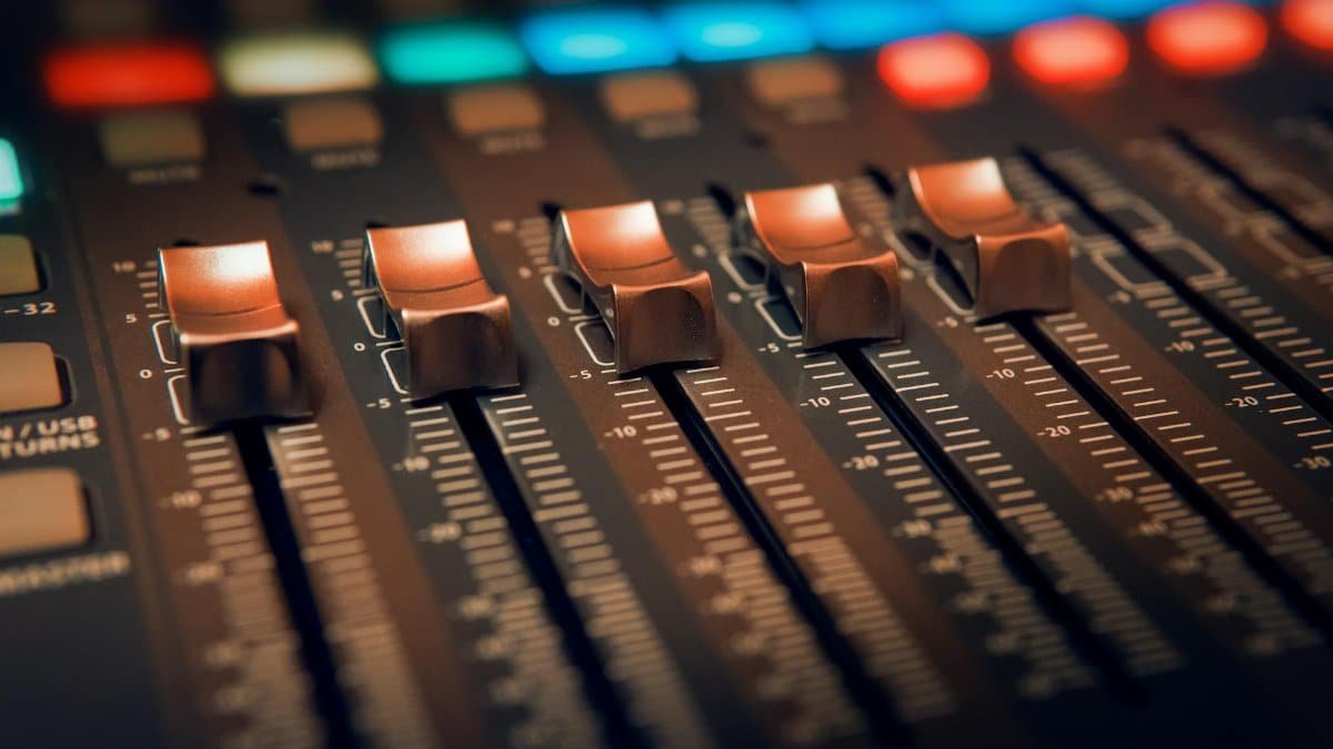 Detailed close-up of an audio mixer with illuminated controls in a studio setting.