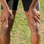 Close-up of an athlete resting after a workout, grasping knees outdoors.