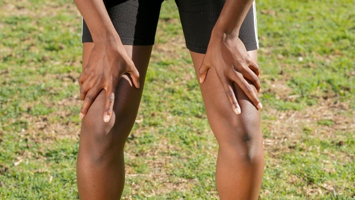 Close-up of an athlete resting after a workout, grasping knees outdoors.