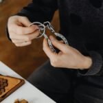 Top view of hands solving metal puzzle, surrounded by wooden brain teasers on a table.