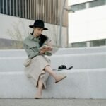 Woman in hat sitting on steps outdoors, writing in a notebook with crossed legs.