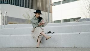 Woman in hat sitting on steps outdoors, writing in a notebook with crossed legs.