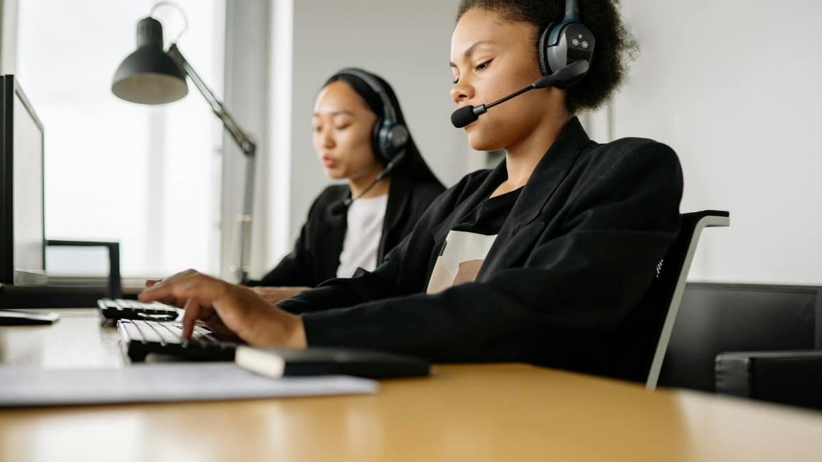 Two call center agents working at desks in an office setting with headsets.