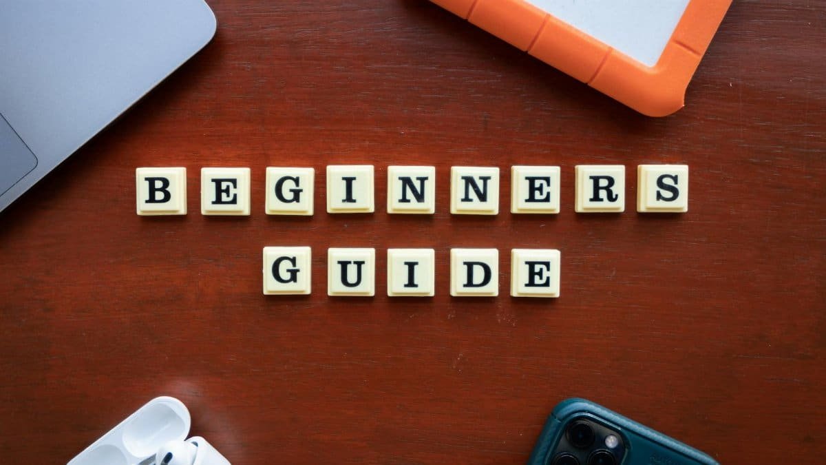 Creative flat lay of gadgets and 'Beginners Guide' text on wooden table.