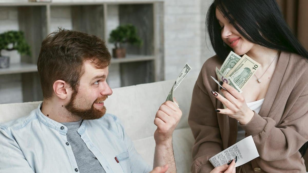A cheerful couple managing their finances at home, holding cash and a receipt.