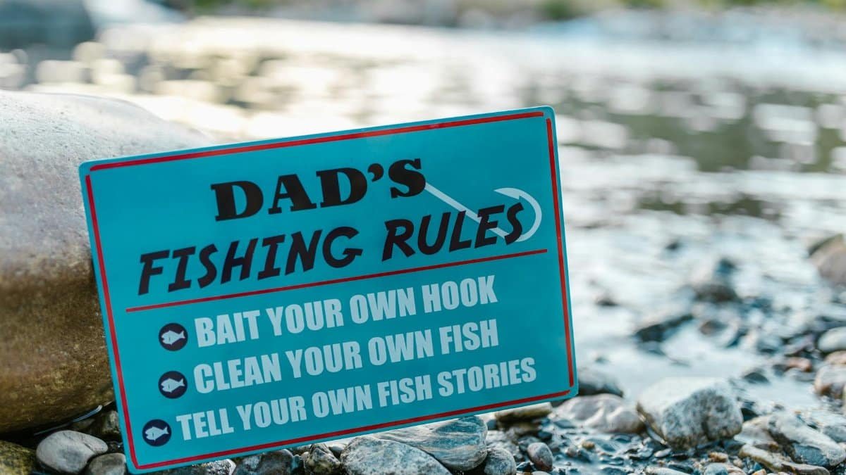 A close-up of a fun sign highlighting dad's fishing rules placed by a river, perfect for Father's Day.