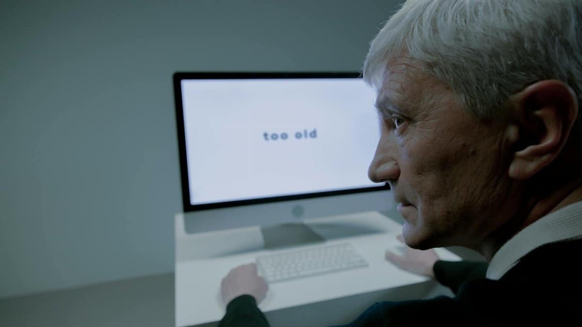 Senior man confronted with ageism on computer screen in job search.