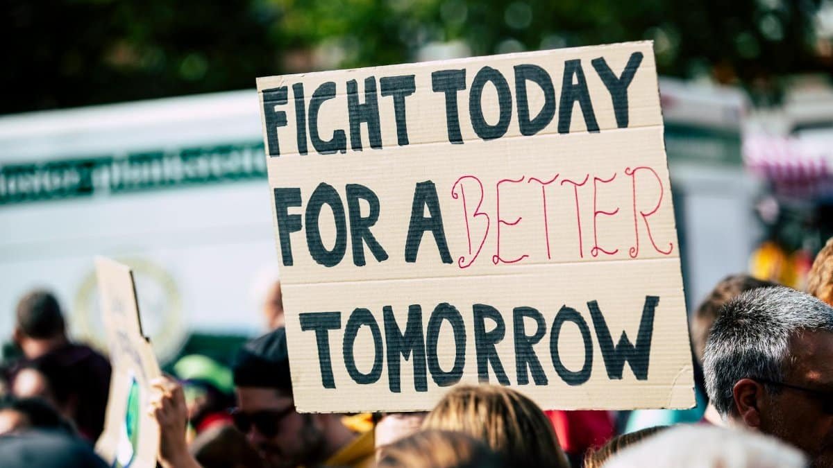 Crowd holding a protest sign with 'Fight Today for a Better Tomorrow', outdoors and during the day.