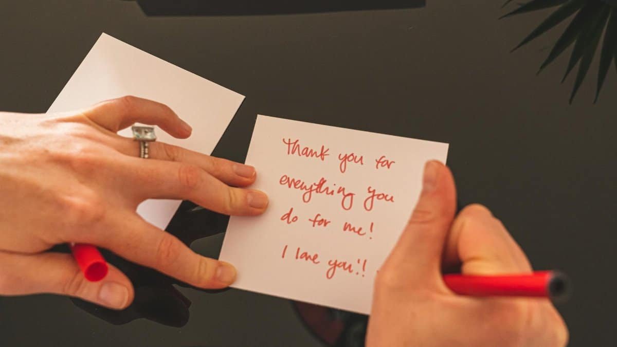 A person writing a heartfelt thank you note with a red pen on white paper.