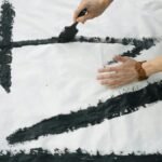 Close-up of artistic Japanese calligraphy being created on a white canvas outdoors.