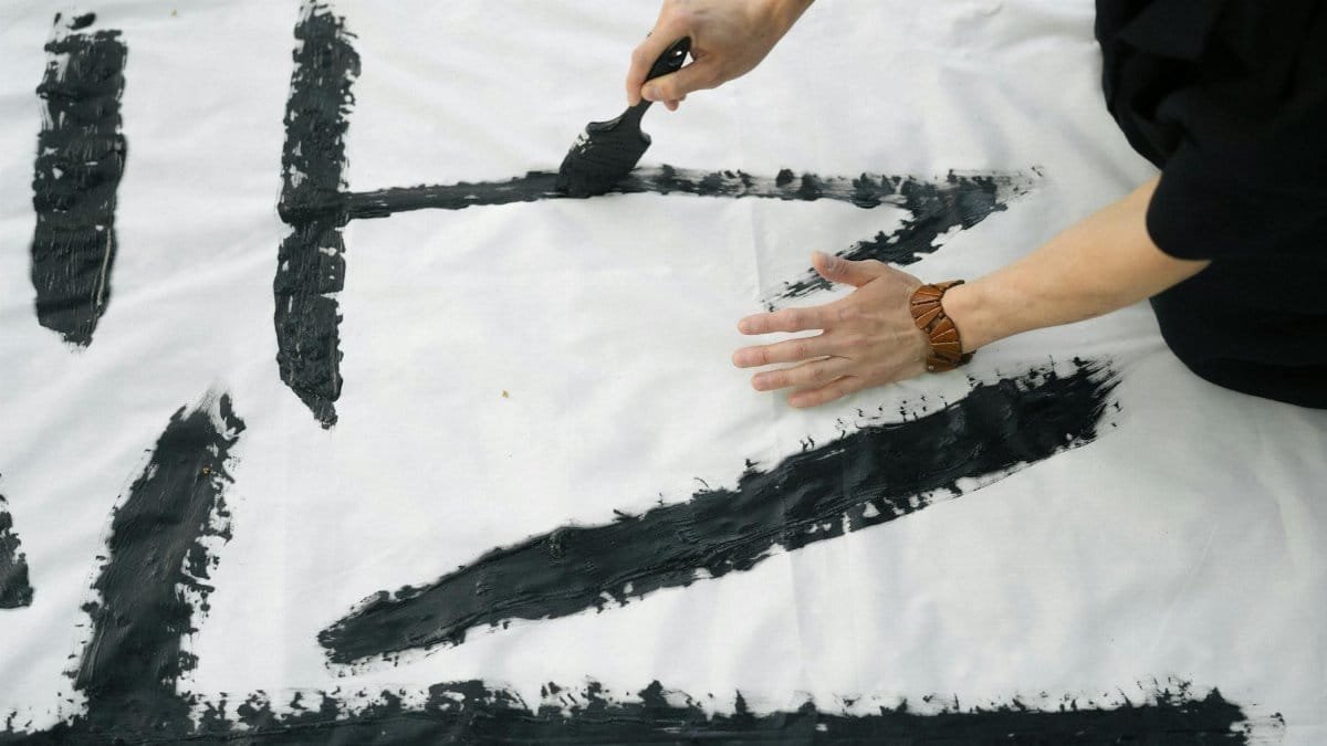 Close-up of artistic Japanese calligraphy being created on a white canvas outdoors.