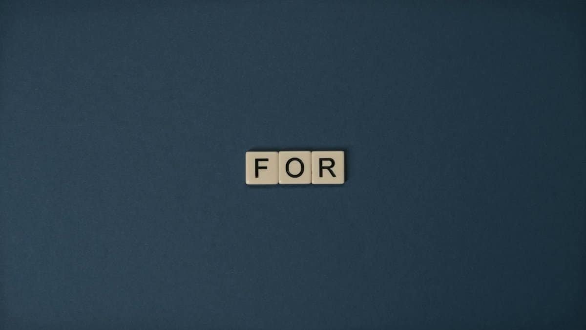 Artistic display of Scrabble tiles spelling the word 'For' on a dark background.