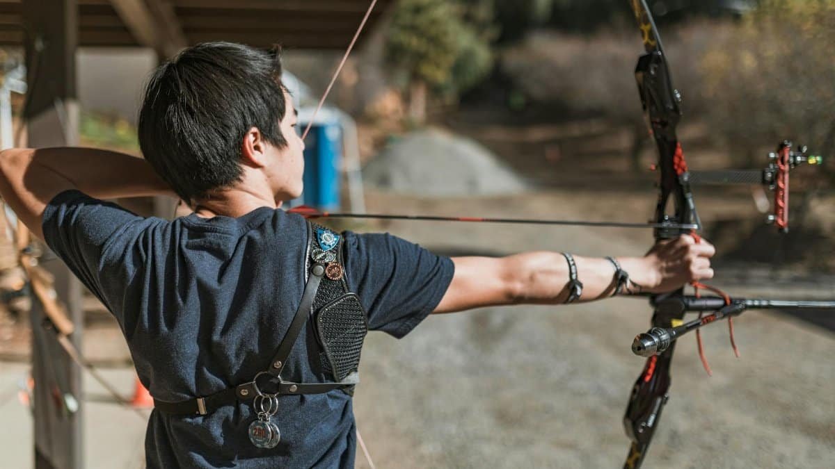 Side view of a man aiming a bow and arrow outdoors, showcasing focus and archery skill.