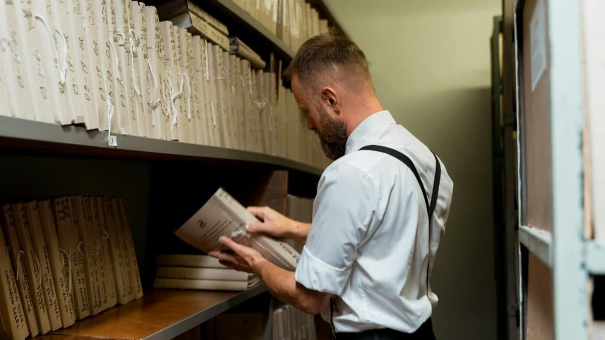 A man in smart casual attire organizing files on shelves in an archive.