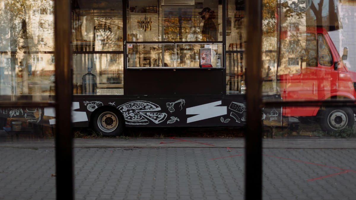 A vibrant food truck parked on a city street, featuring artistic designs and reflections.