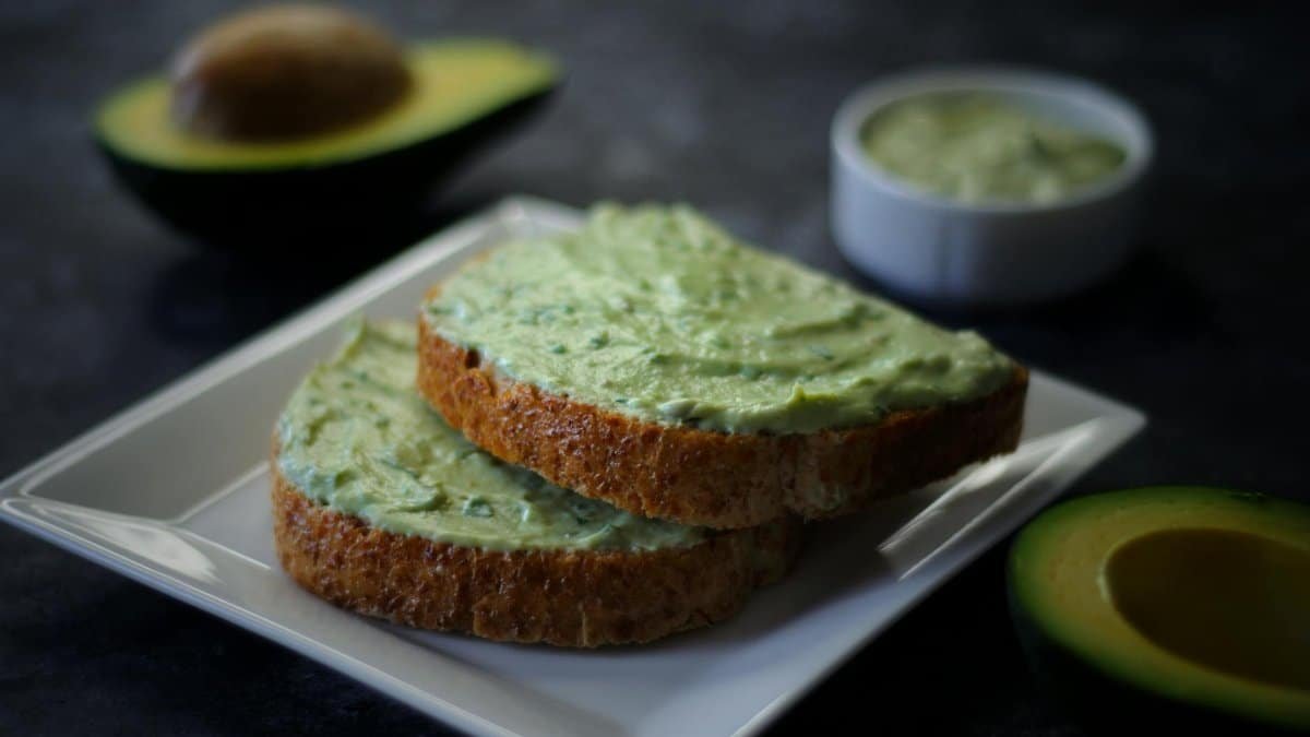 Delicious avocado spread on toast with fresh avocado halves and a dipping sauce.