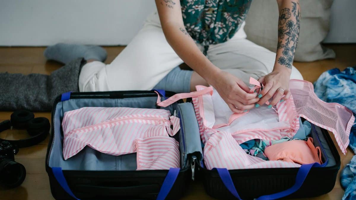 A woman packing her travel suitcase on the floor indoors, preparing for a trip.