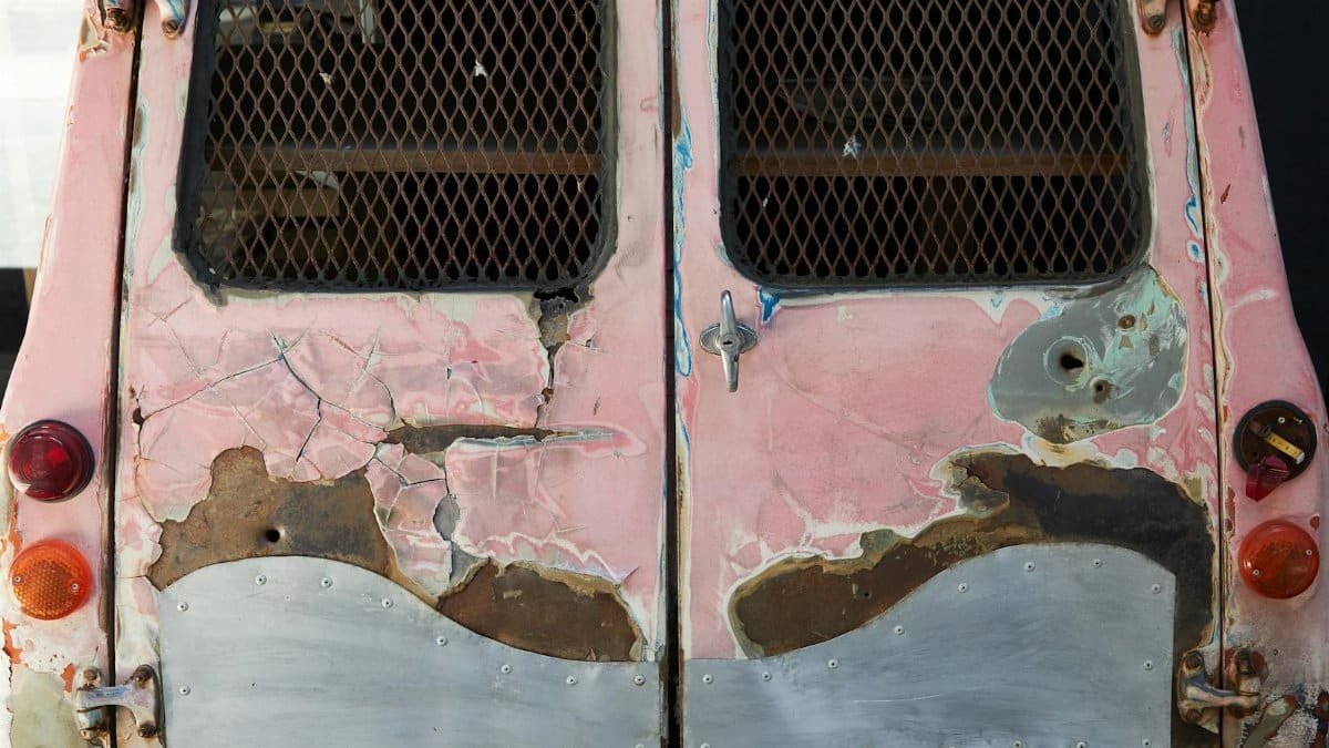 Old automobile with broken taillights and windows with lattice covered with rust and scratches
