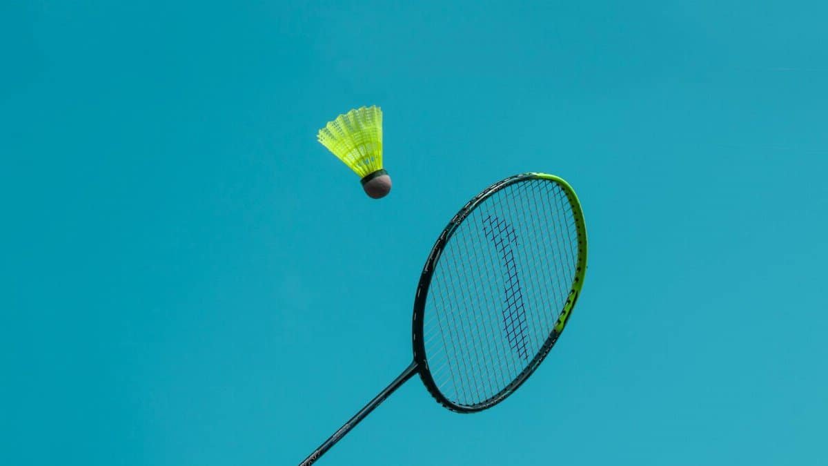 A thrilling action shot of a badminton racket hitting a shuttlecock against a clear blue sky.
