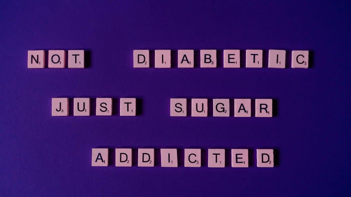 Scrabble tiles spell out a humorous message on a vivid purple background, highlighting sugar addiction.