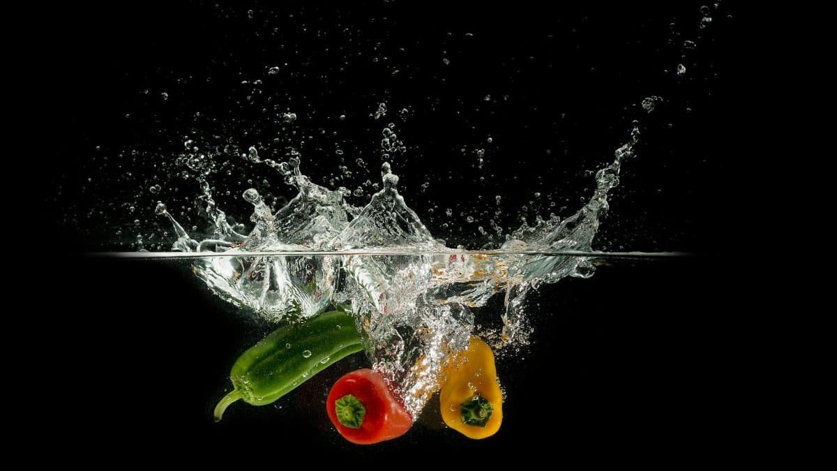 Colorful bell peppers splashing in clear water against a dark background.