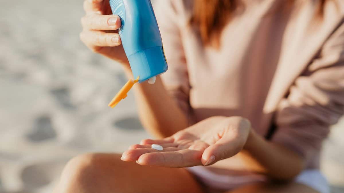 A person applies sunscreen at the beach on a sunny day.