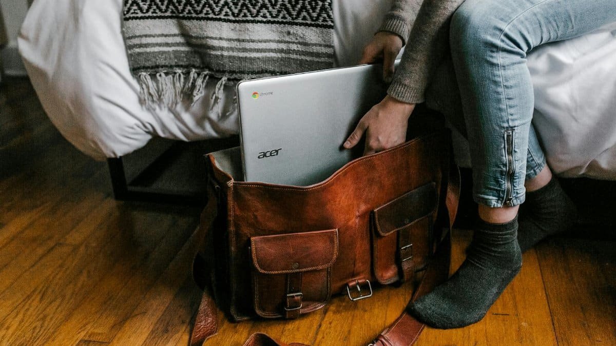 A young woman packs a laptop into a leather bag, embodying remote work lifestyle.