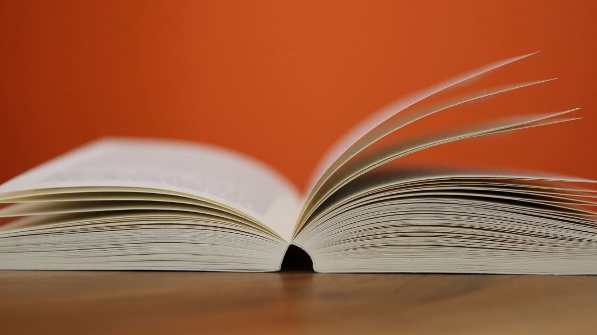 An open book with pages turning against a vibrant orange background, symbolizing knowledge and education.