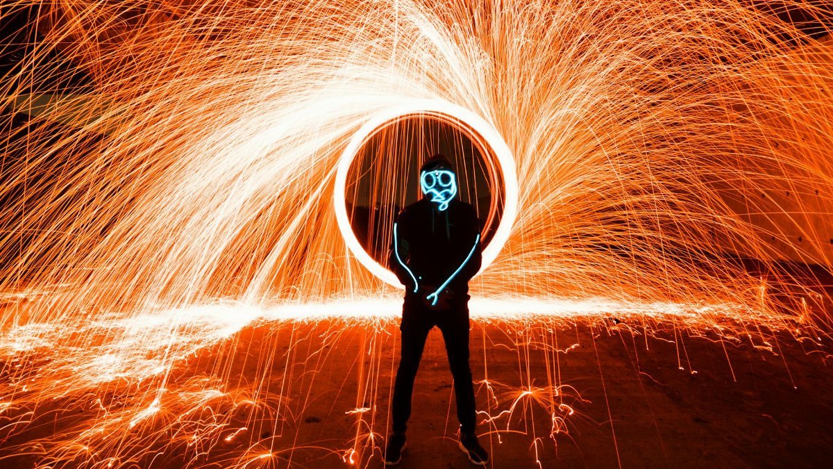 A person creates sparks with a steel wool light painting, resulting in a dynamic and colorful scene.