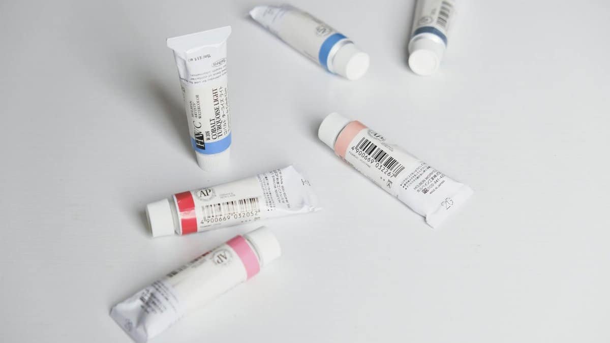 Close-up of colorful paint tubes arranged on a white surface in a flat lay style.