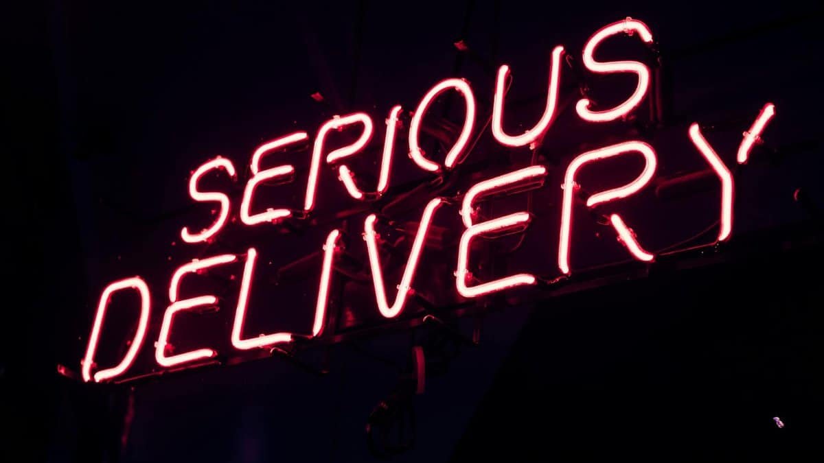 Bright pink neon sign displaying 'SERIOUS DELIVERY' at night, perfect for urban aesthetics.