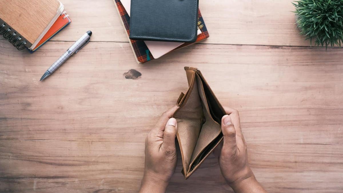 Top view of hands holding an open empty wallet on a wooden desk with notebooks and pen.