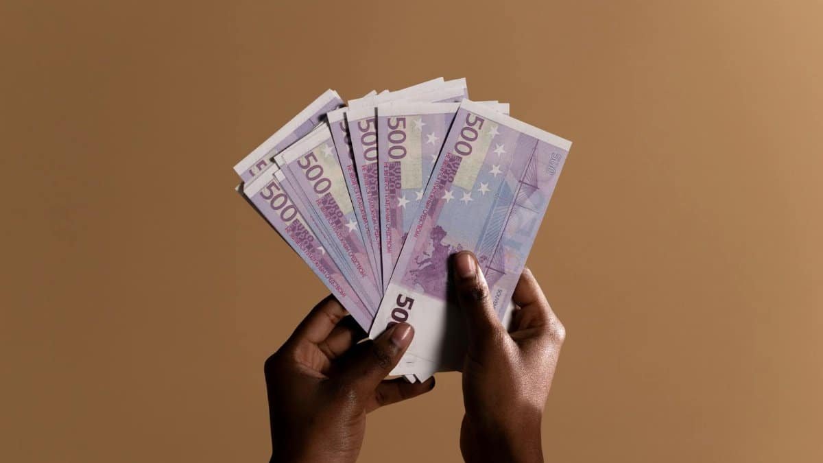 Close-up of hands holding several 500 euro banknotes against a neutral beige background, concept of wealth.