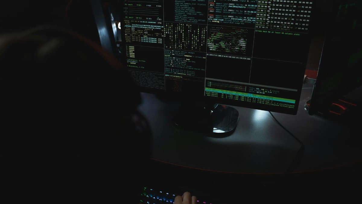 Dark room setup with code displayed on PC monitors highlighting cybersecurity themes.