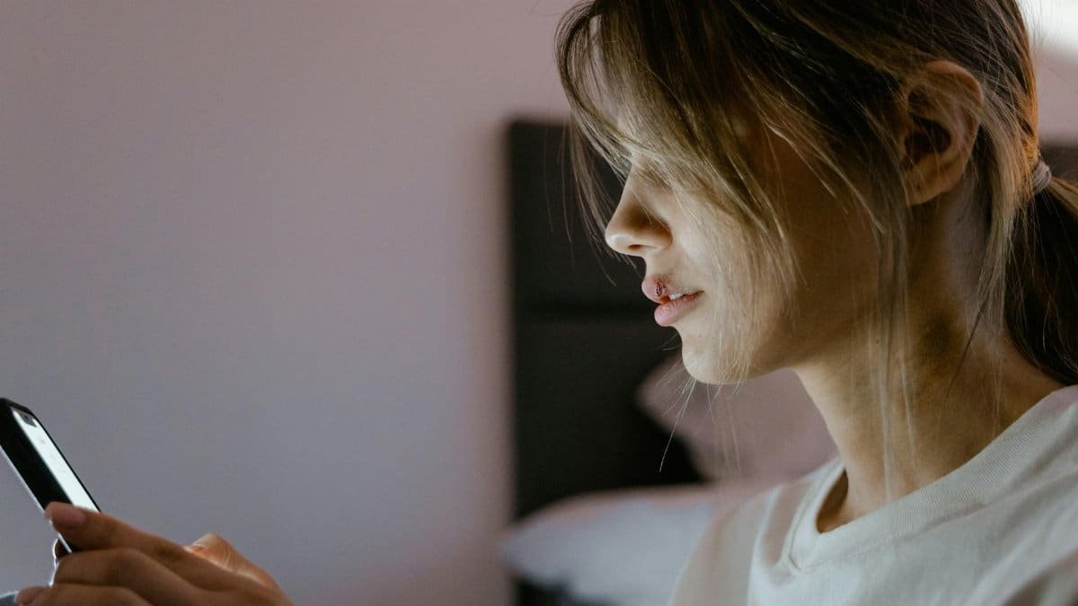 Profile of a young woman attentively using her smartphone indoors, lit by screen light.