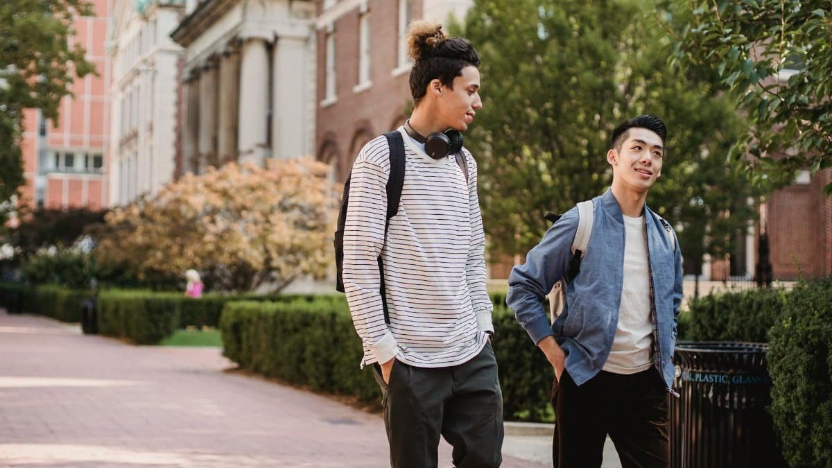 Friends enjoying a walk on a sunny university campus, chatting and spending time together.