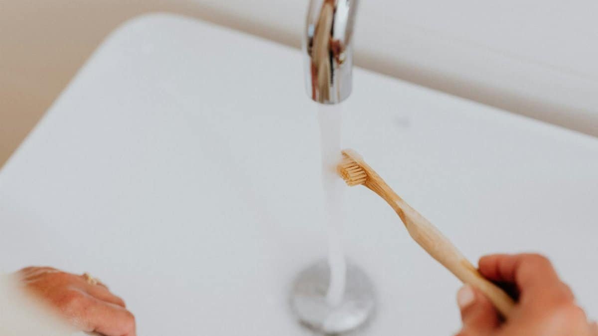 Close-up of a bamboo toothbrush under a running faucet, promoting sustainable living.