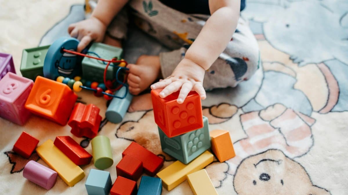 Toddler engaging with vibrant toy blocks on a patterned rug in a playful setting.