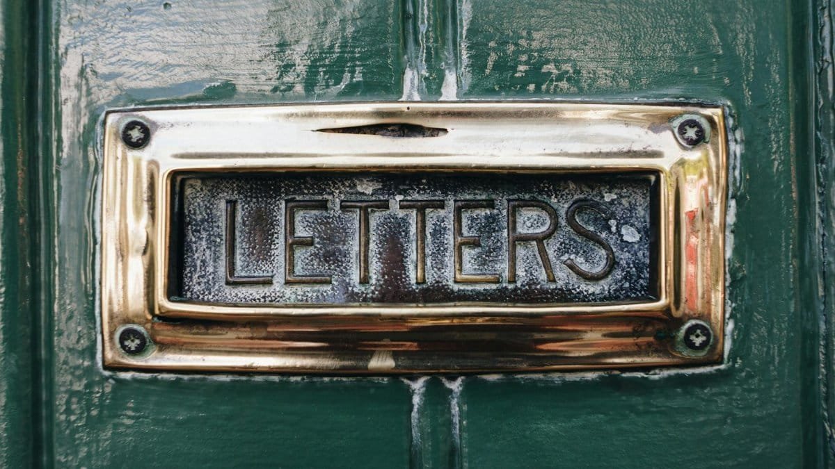 Close-up of an antique mail slot labeled 'letters' on a painted green door.