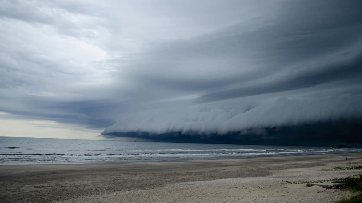 A dark storm cloud formation looms over a tranquil, deserted beach, showcasing nature's power.